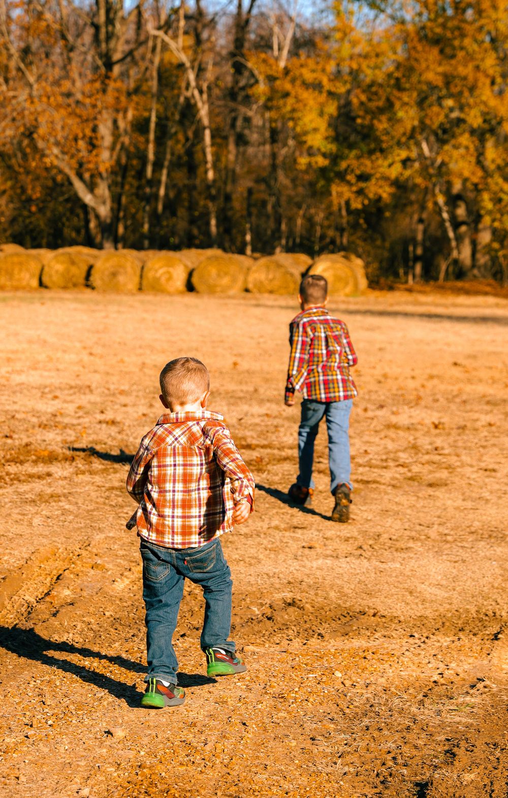Two people in matching plaid shirts explore a rustic outdoor area with hay bales in the background.