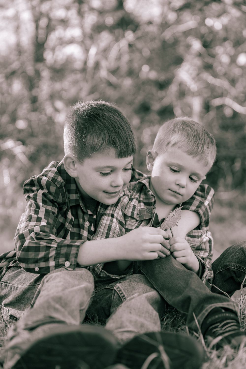 Two children sit closely together examining something in black and white photography.