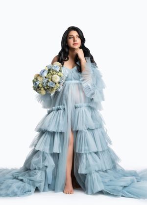 Ethereal powder blue tulle gown with tiered ruffles and sheer sleeves paired with a white and blue floral bouquet.