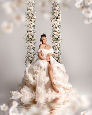 Elegant maternity portrait on a floral swing with white rose columns and dreamy reflection in water.