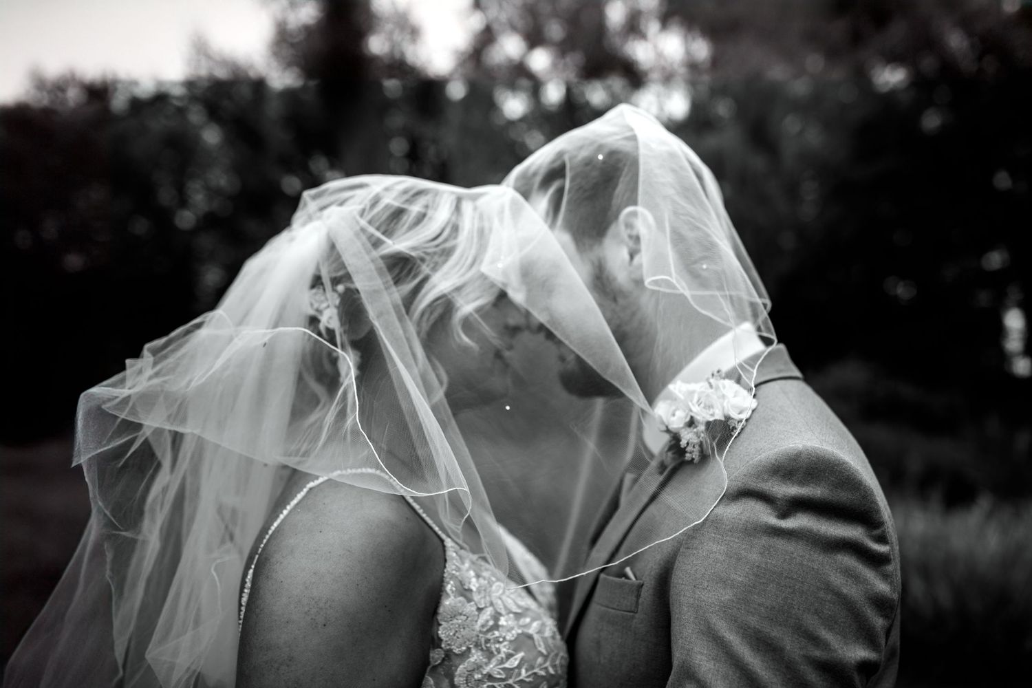 Artistic black and white photo of a couple sharing an intimate moment under a flowing veil. Essex wedding photographers. Houchins venue