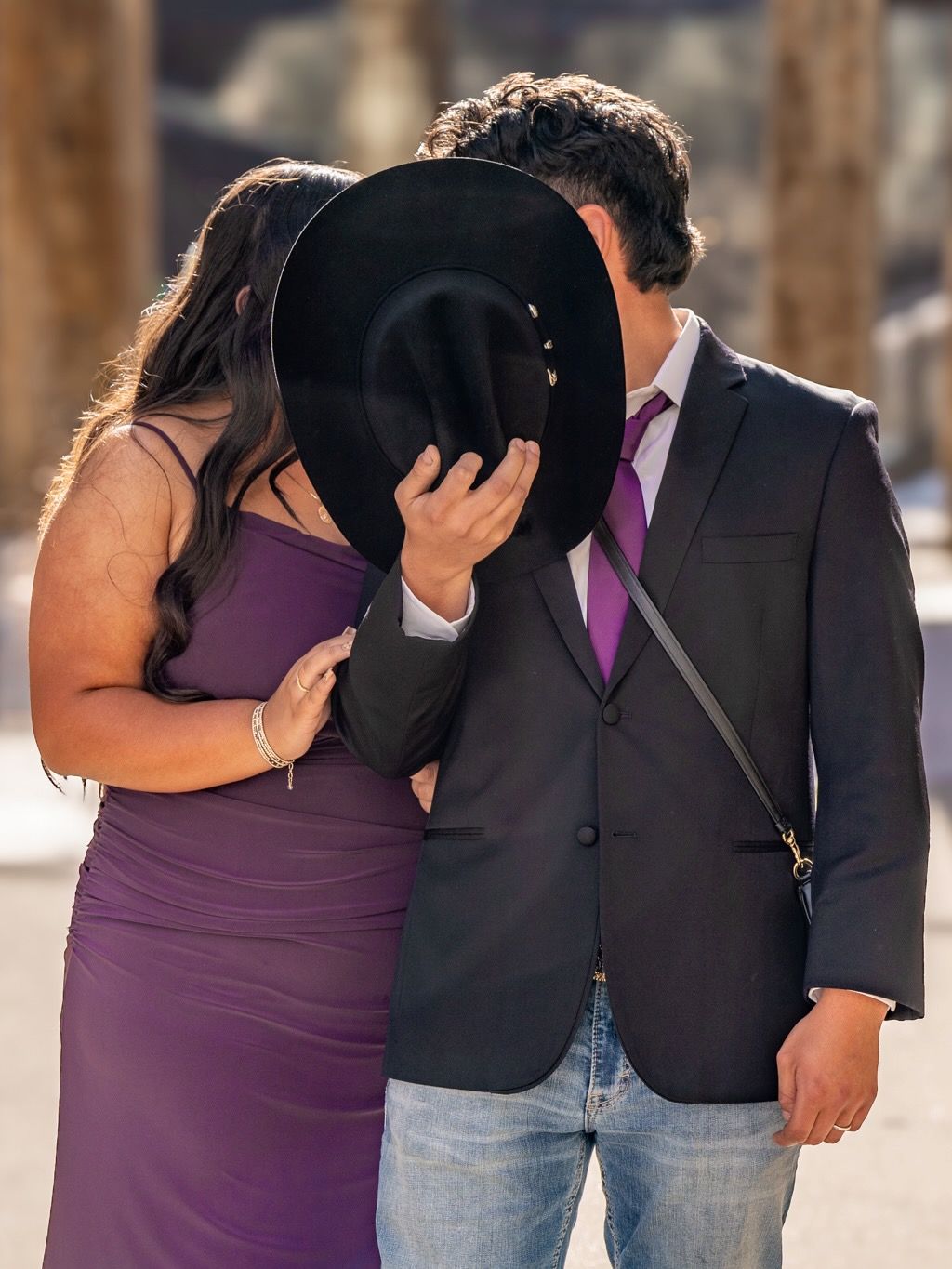 Couple in formal attire sharing intimate moment behind black hat.