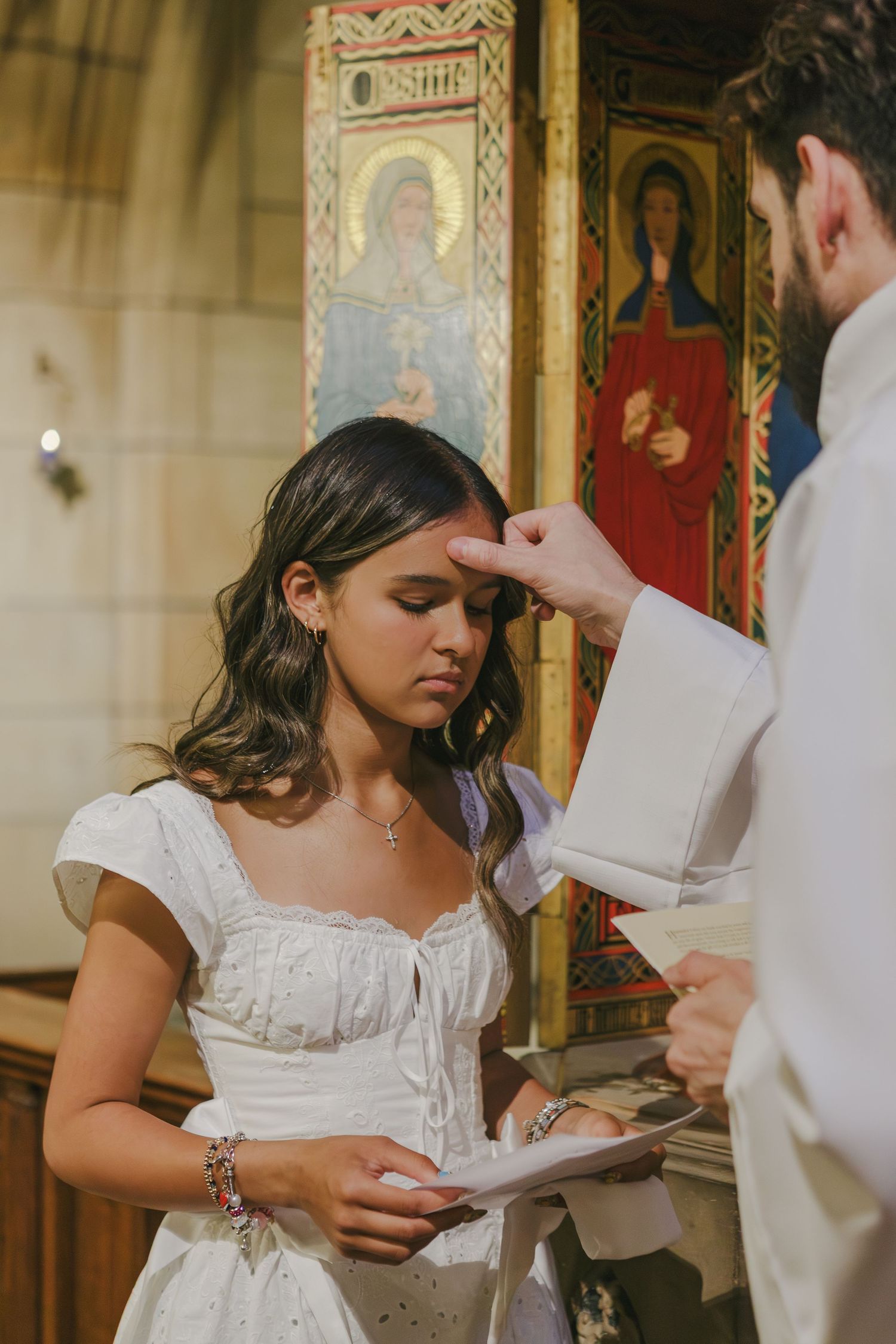 Priest applies sacred oil to baptism girl’s forehead during NYC ceremony by NYC family photographer Paula Brearley