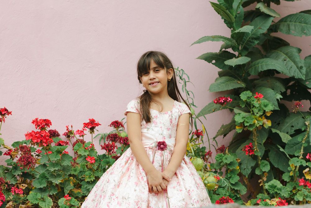 Boy's sister in pink dress with red flowers in the background by NYC family photographer Paula Ortiz.