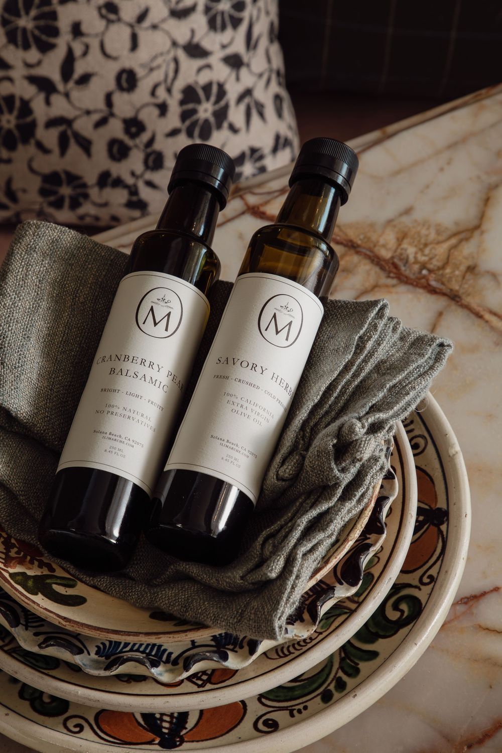 Luxury skincare bottles arranged on decorative plates with gray linens against a marble surface in moody lighting.