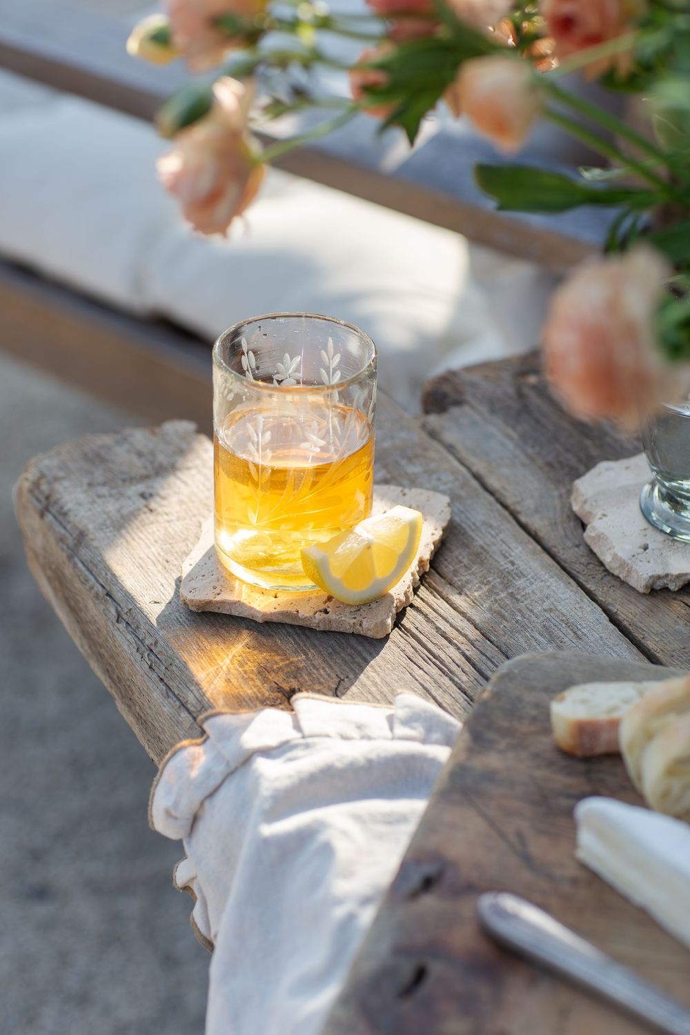A glass of golden beer with lemon slices sits on a rustic wooden surface with soft peach flowers in the background.