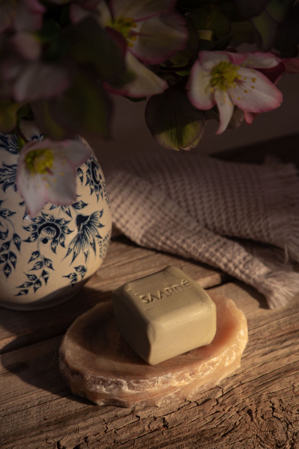 Artisanal soap bar on wooden dish with delicate cherry blossoms and blue-and-white porcelain vase in soft lighting.