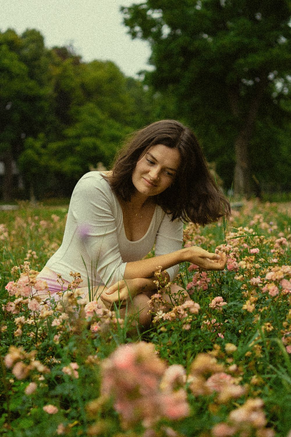 Portrait Fotoshooting im Spätsommer einer hockenden Frau im Blumenfeld im Blüherpark Dresden, die sich durch die Haare fässt.
