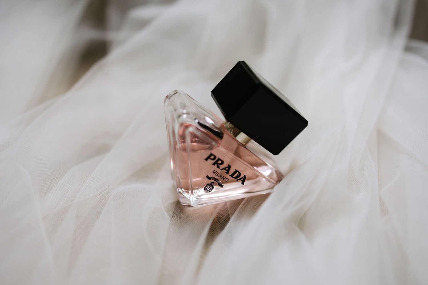 A pink perfume bottle with black cap sitting on white tulle fabric background.
