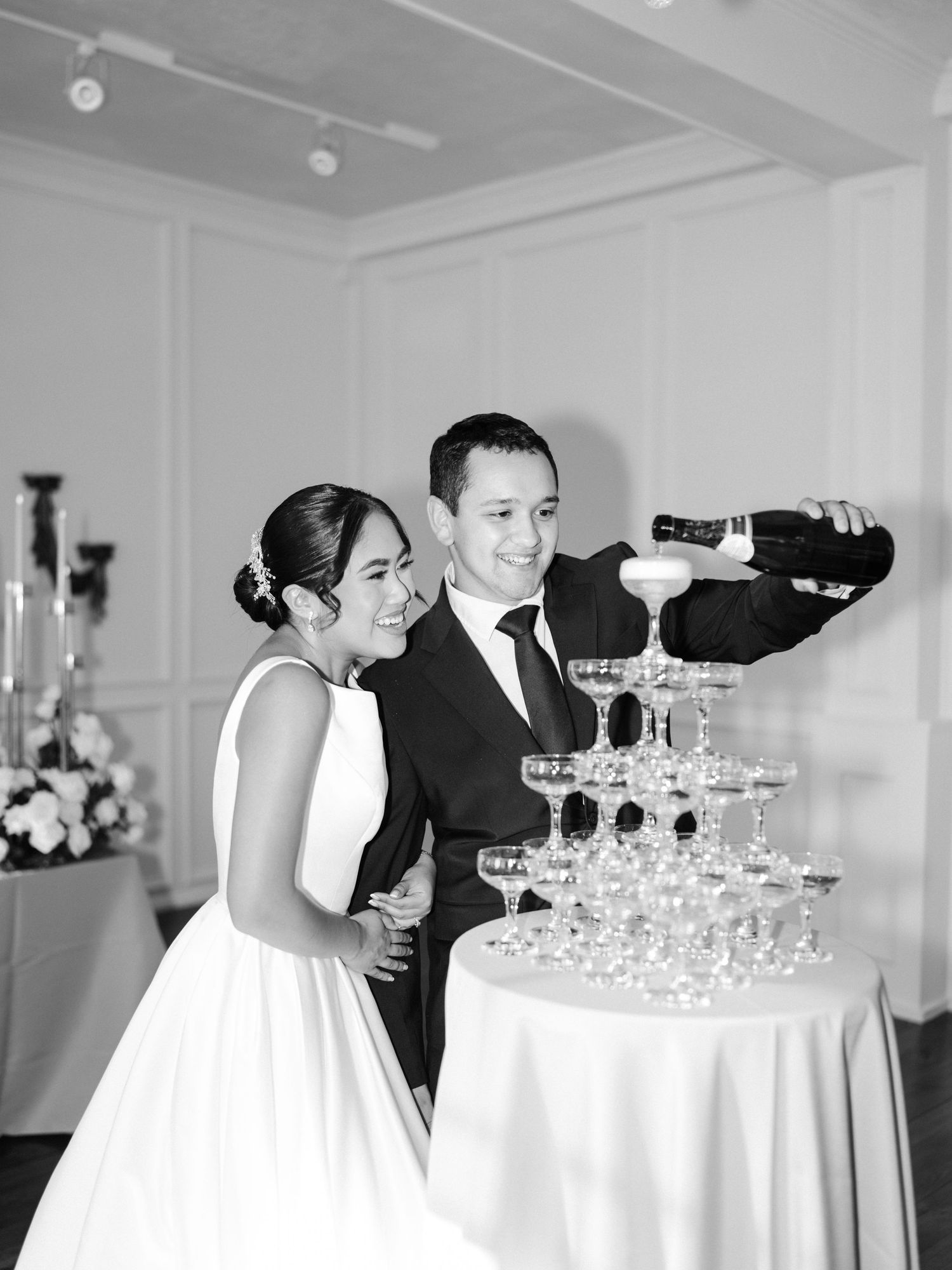 A couple pours champagne into a tower of glasses at their elegant black and white wedding reception.