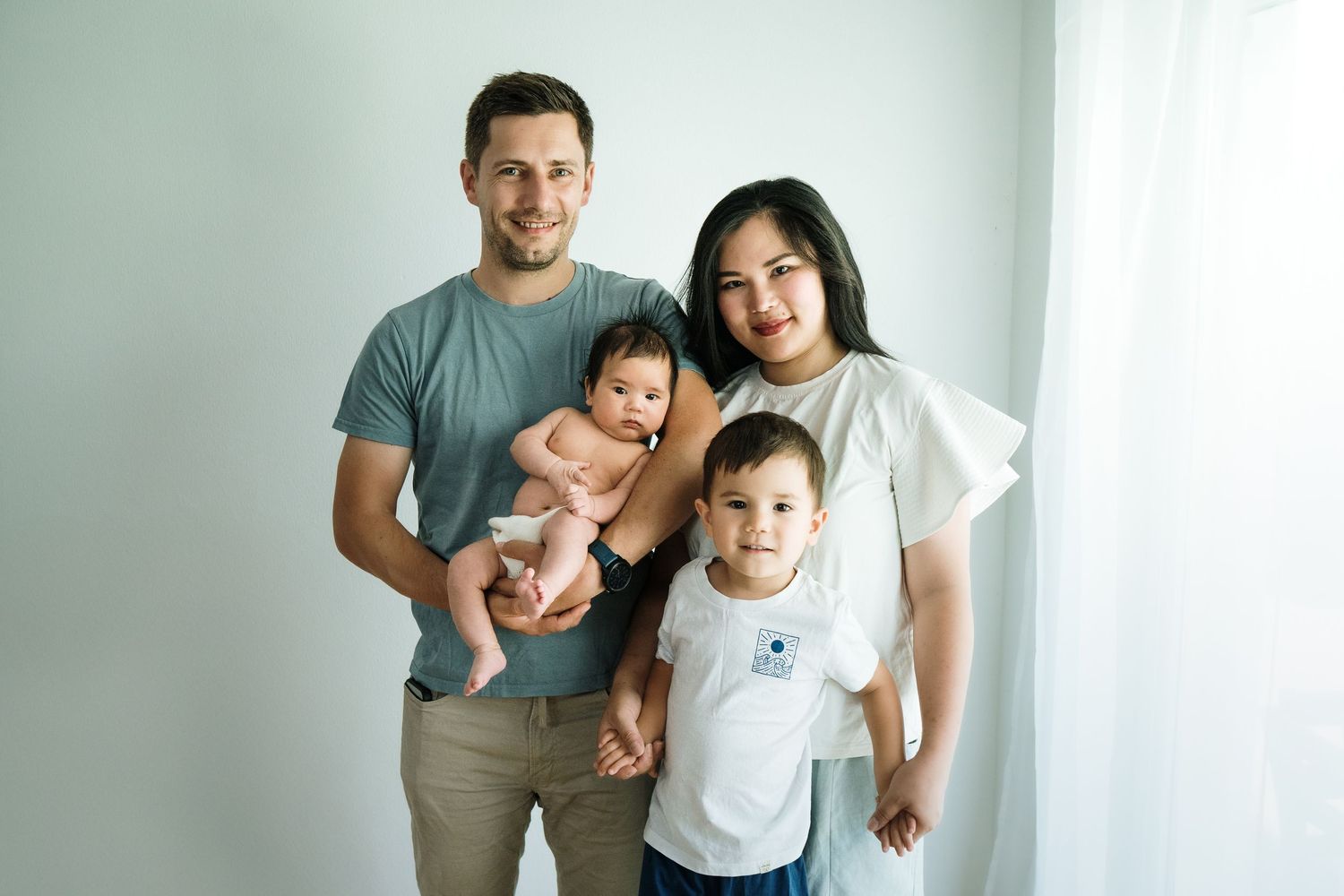 Family portrait against white wall in casual attire.