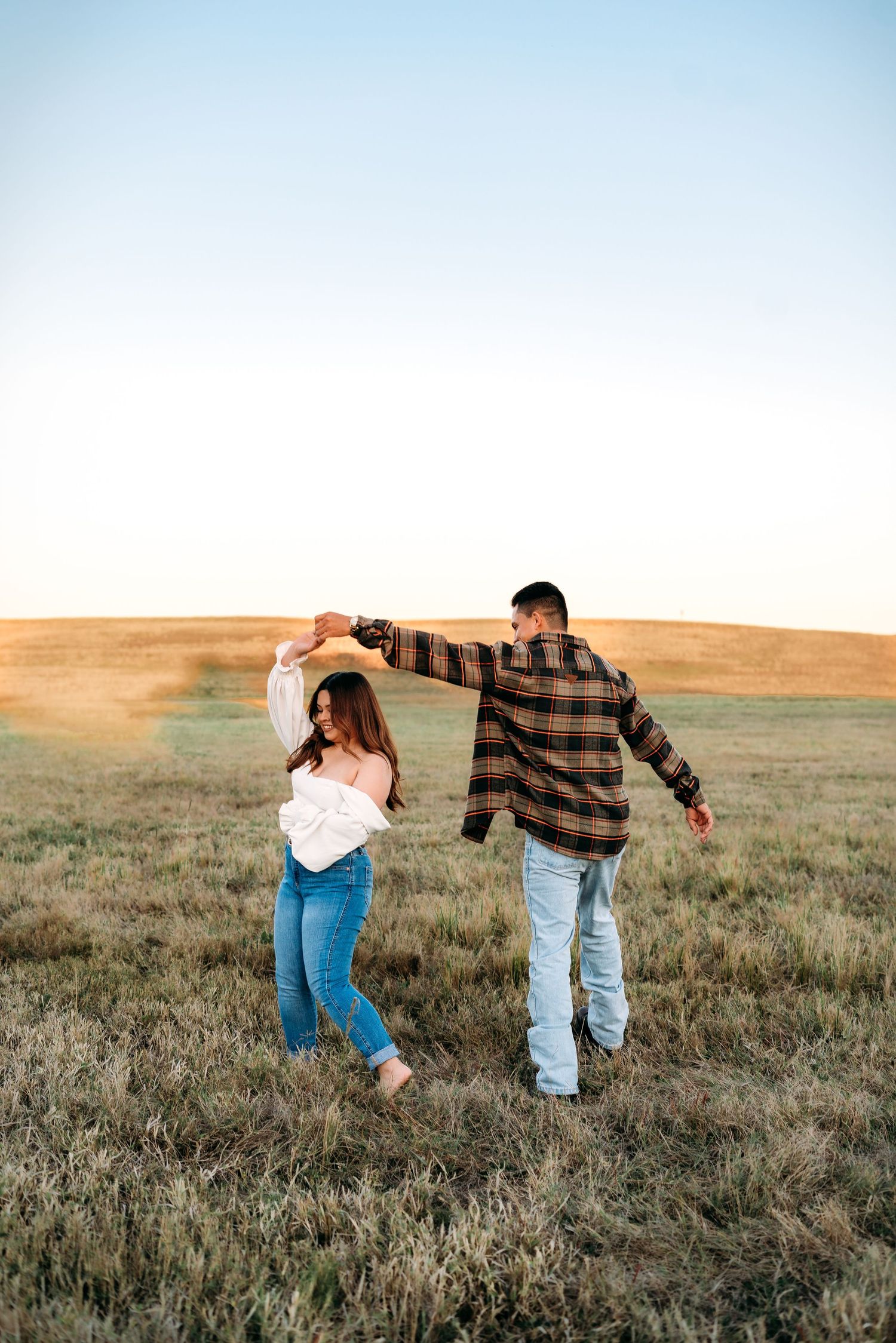 Gentleman twirling woman in a green field as they dance.