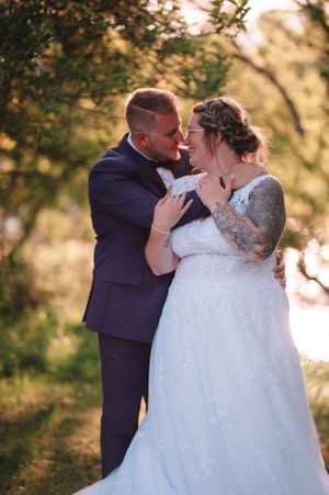 Romantic wedding couple sharing an intimate moment in golden sunlight with natural foliage backdrop.