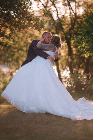 Newlyweds embrace in a romantic dip pose against a sunset-lit garden setting.