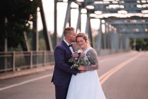 Wedding couple poses on a bridge at dusk with bouquet.