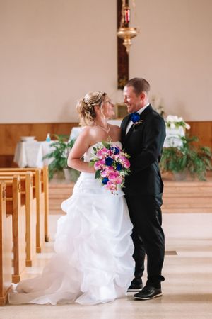 Wedding couple poses in church aisle with cascading pink and blue floral bouquet.