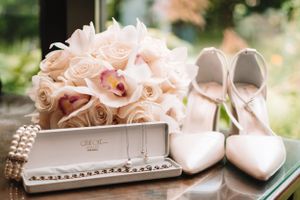 Wedding detail shot of white heels, roses and jewelry box on wooden surface.