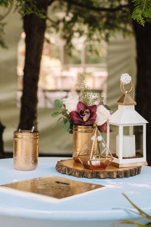 Rustic wedding centerpiece with mason jars, lantern and wood slice on white tablecloth.