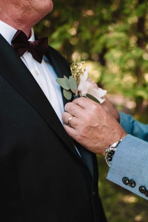 Close-up of boutonniere being pinned to groom's lapel.