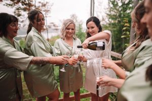 Bridesmaids in sage robes pouring champagne during pre-wedding preparations.
