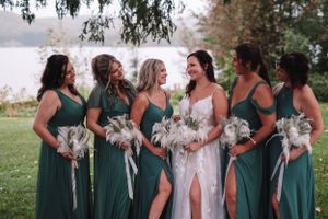 Bridesmaids in elegant green dresses holding white bouquets pose together outdoors.