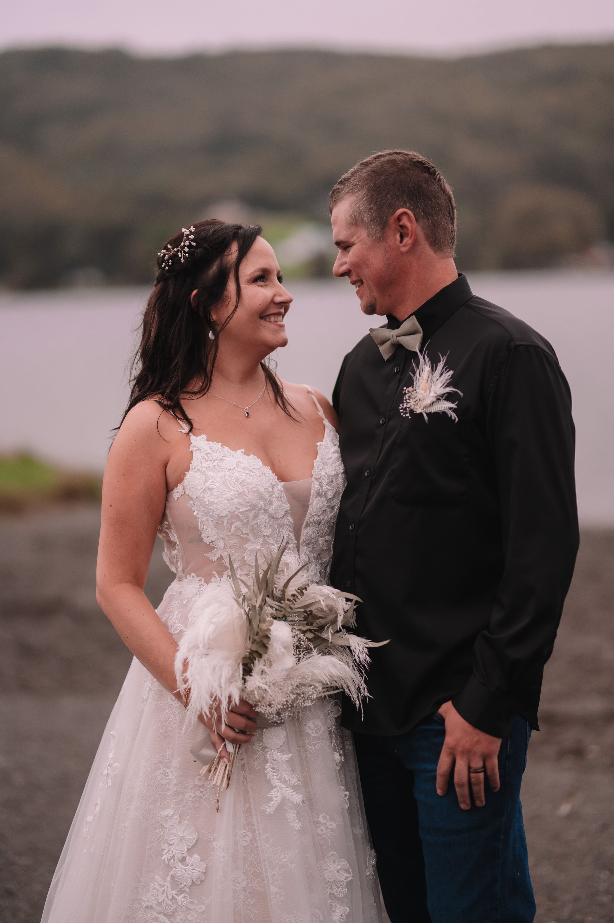 A tender moment between newlyweds on a rocky shore with a lake in the background.