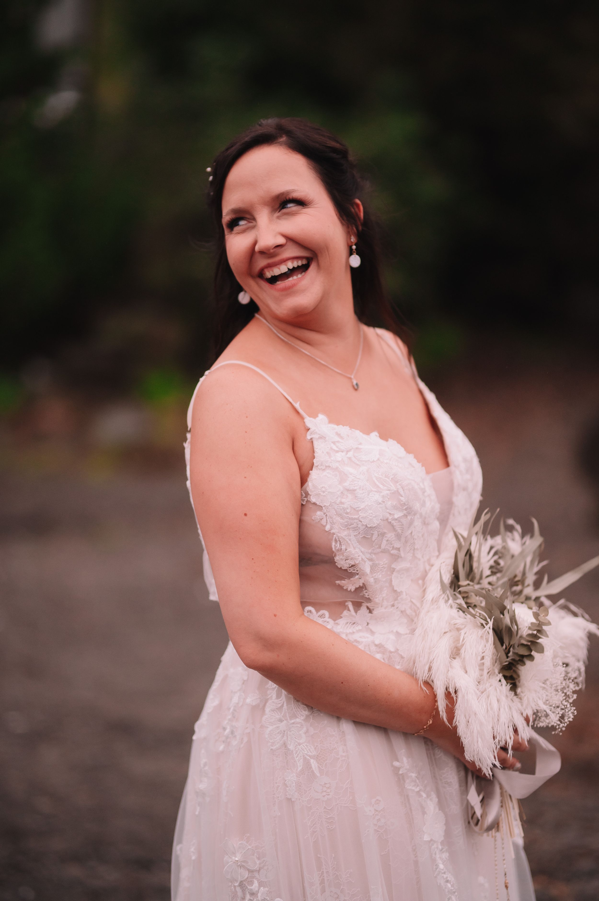Radiant bride in lace wedding dress holding a white feather bouquet.
