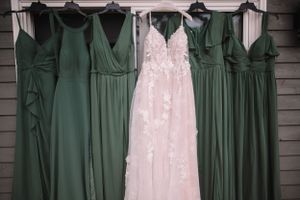 Wedding dress and sage green bridesmaid dresses hanging on display.