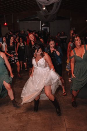 Wedding party dancing on a dark dance floor with the bride wearing cowboy boots.