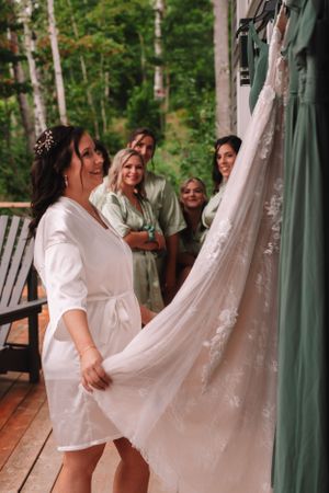 Pre-wedding moment with bride and bridesmaids admiring wedding dress on outdoor deck.
