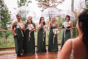 Bridesmaids in sage green dresses holding clear umbrellas on rainy wedding day.