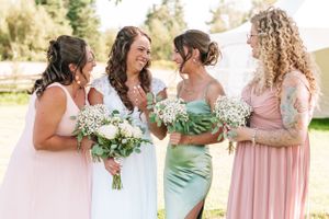 Bridesmaids in pink and mint dresses laughing together while holding floral bouquets.