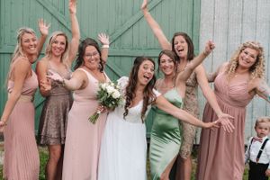 Fun group photo of bridal party in pink and green dresses posing excitedly against barn door.