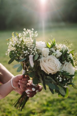 White rose and baby's breath wedding bouquet held in sunlight with dreamy bokeh background.