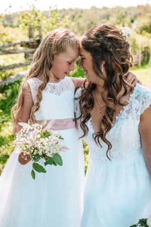 Tender moment between bride and flower girl sharing an intimate moment outdoors with bouquet.