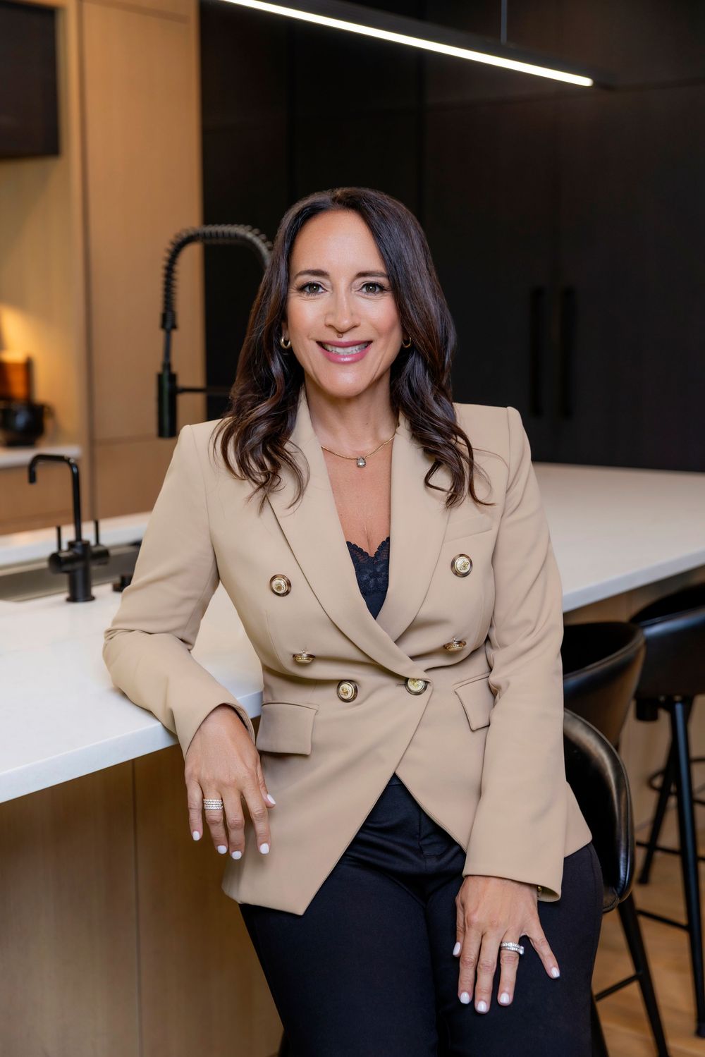 Professional business portrait of someone wearing a beige blazer and black top in an office setting.
