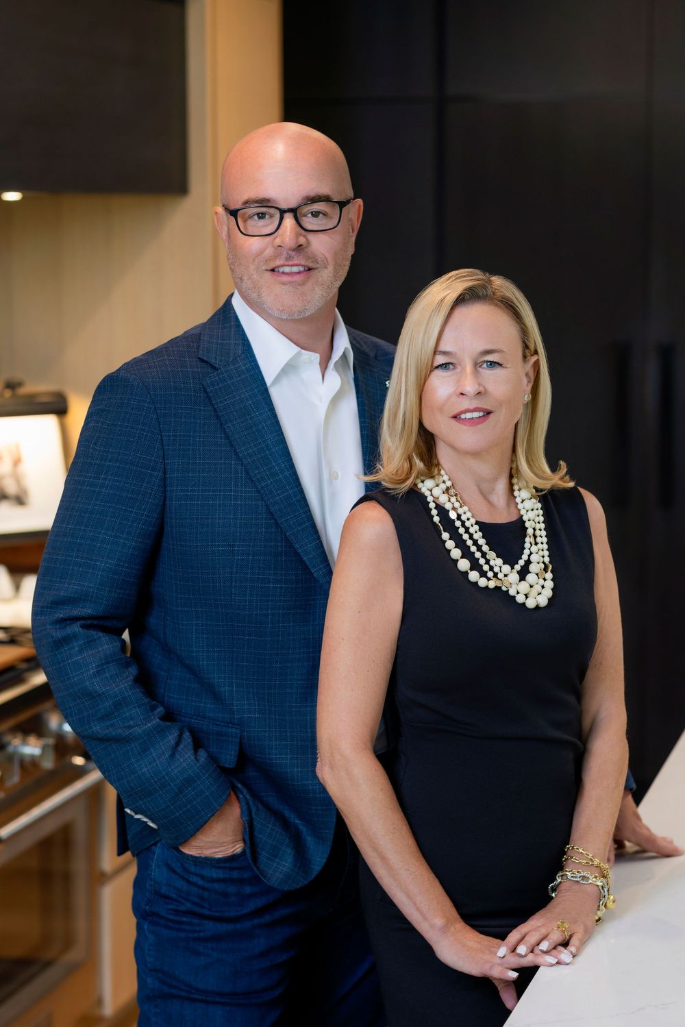 Professional business couple poses together in modern office setting wearing coordinated navy and black attire.