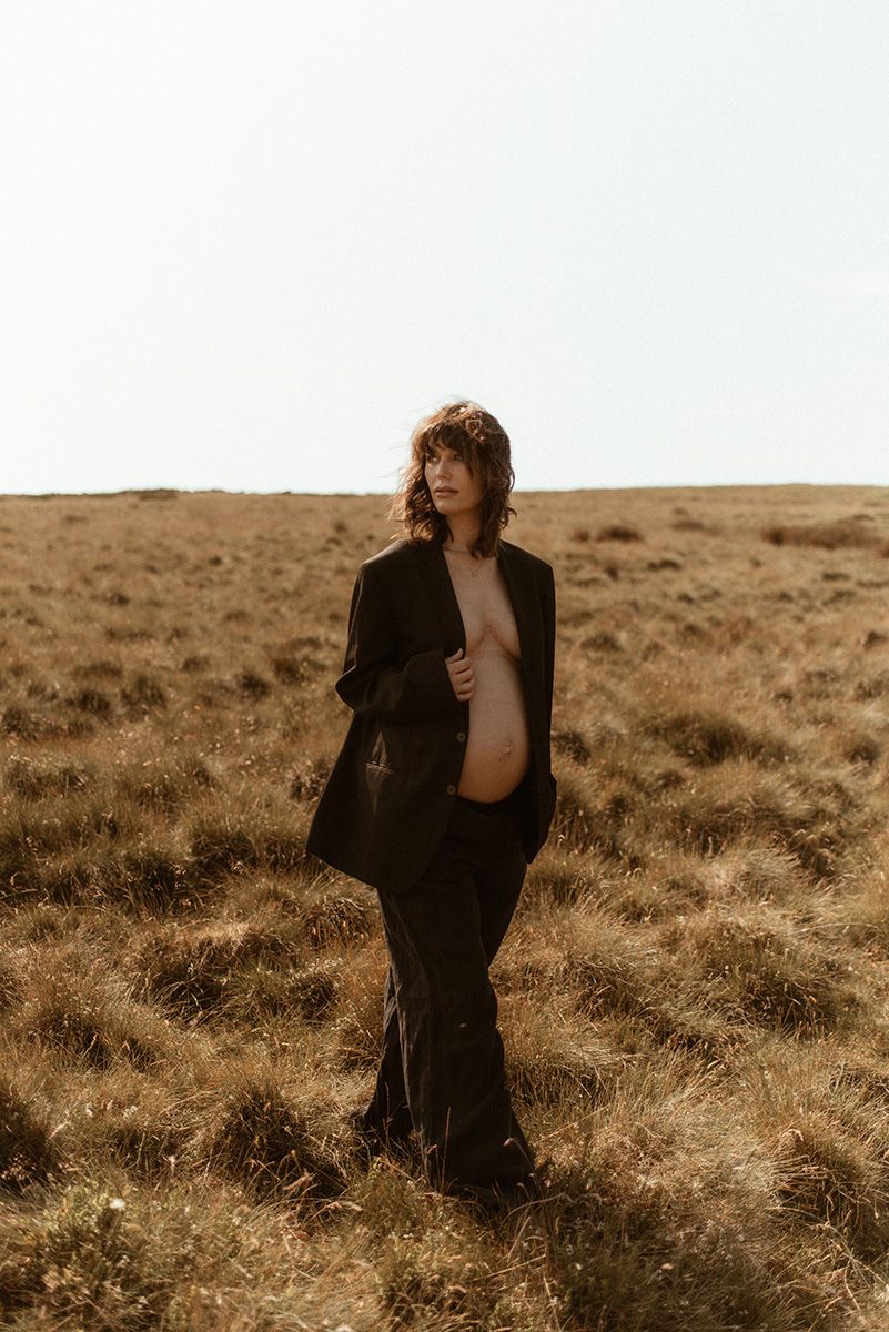 Artistic portrait in earthy tones of person wearing black clothing standing in golden grass field at sunset.
