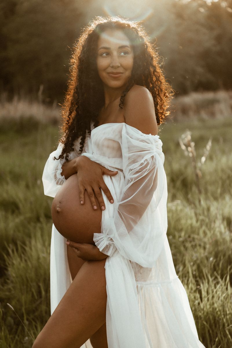 A maternity photo shows an expectant mother in a white flowing dress posing outdoors in golden sunlight.