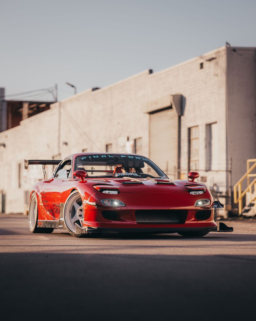 Red sports cars lined up against industrial building exterior in dramatic lighting.