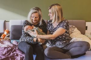 3-Generationen Foto einer Wochenbettreportage, es ist zu sehen wie die Mutter das neugeborene Baby der Oma reicht.