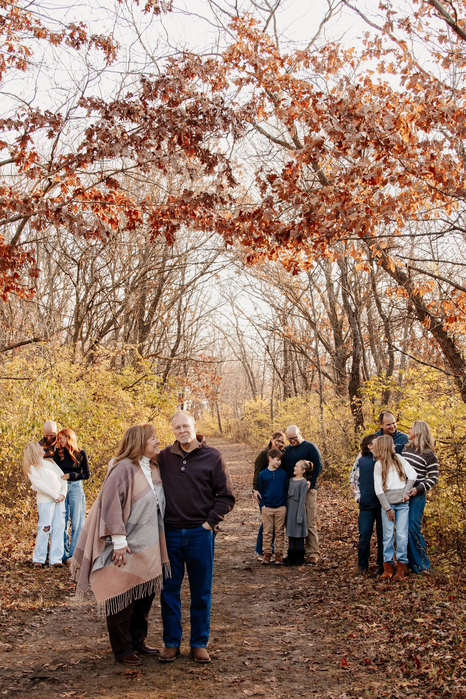 Extended family photos gathering under autumn trees with fall foliage on a forest path.