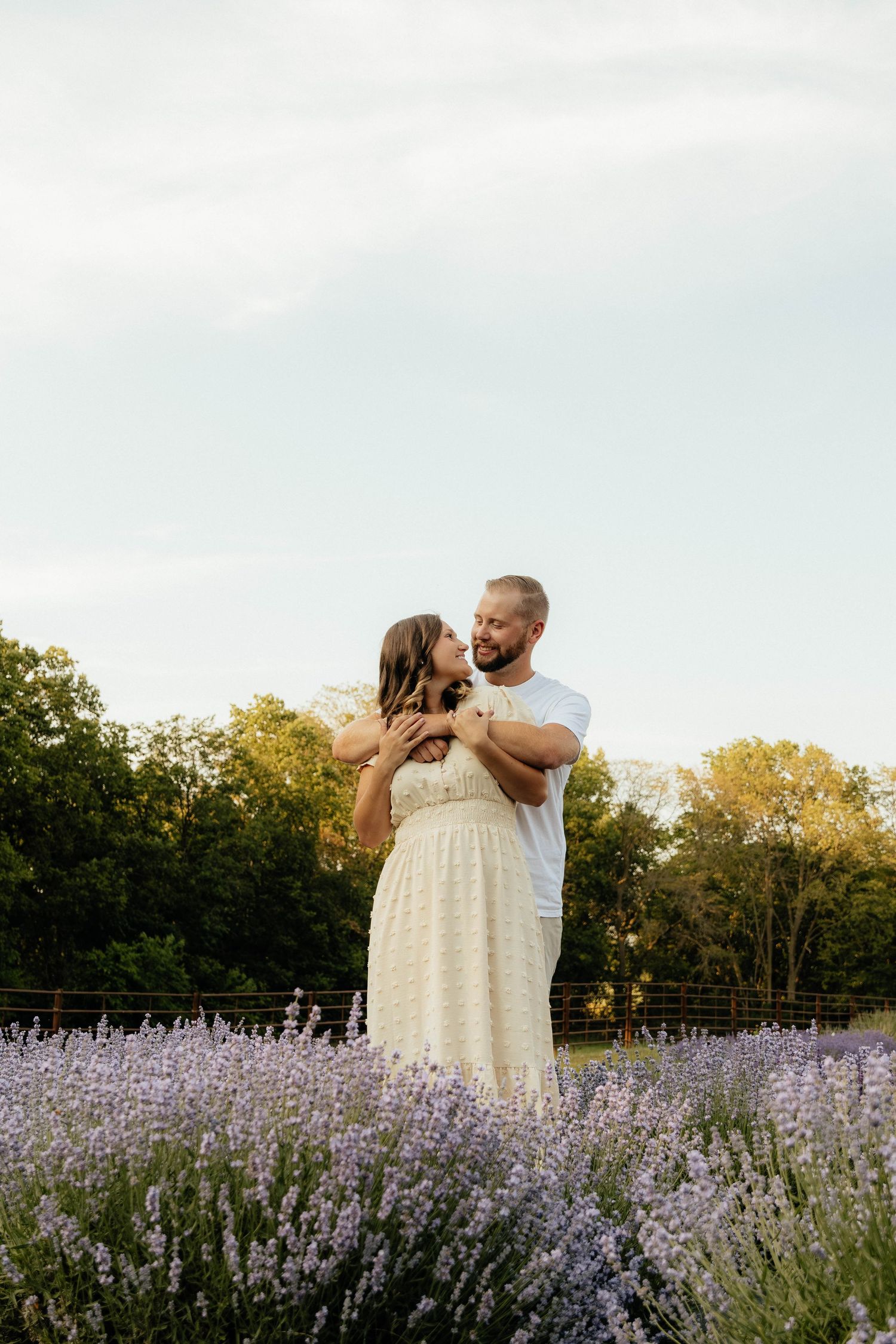 A couple taking engagement photos for their wedding in Iowa embraces in blooming lavender field during golden hour.