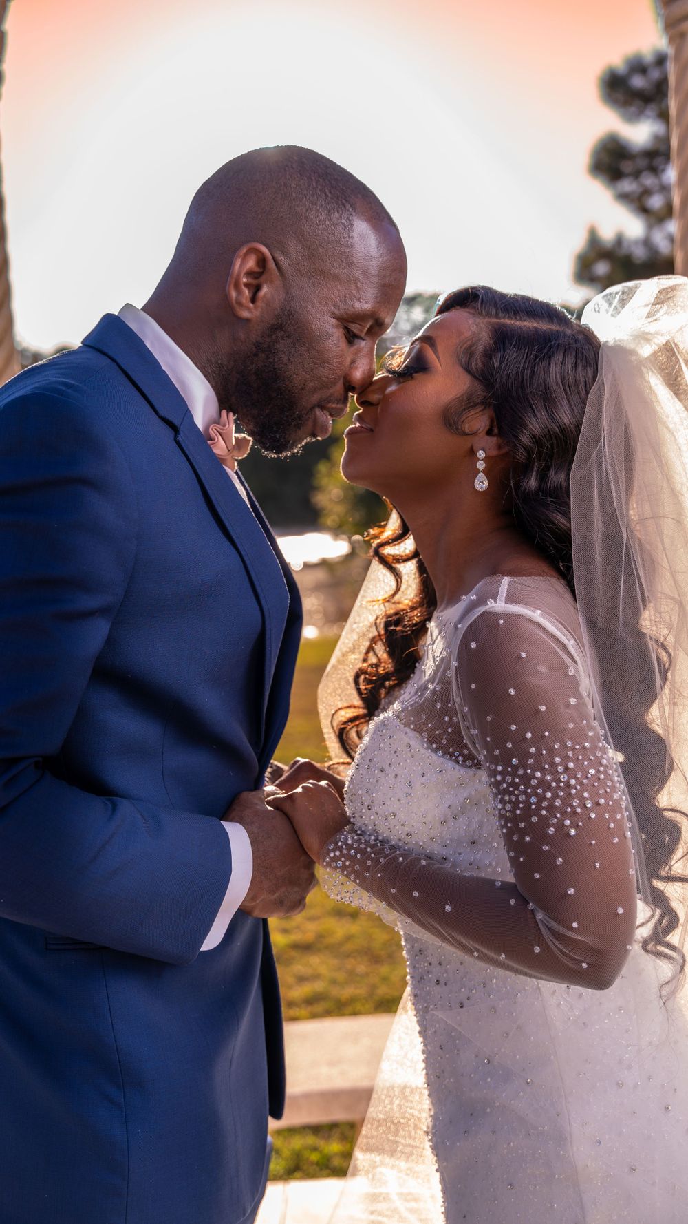 A romantic moment between newlyweds as they share their first kiss in elegant wedding attire outdoors.