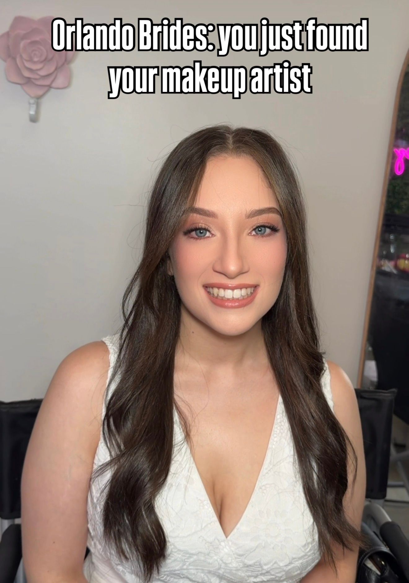 Young brunette woman in white dress smiling, promoting Orlando bridal makeup artist services.