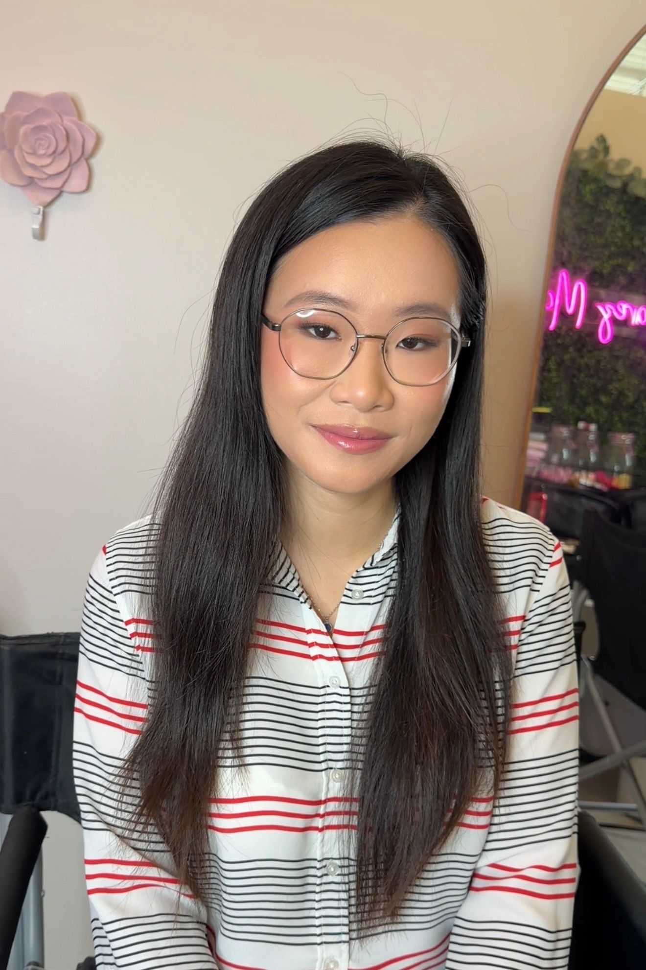 Young woman with long dark hair and glasses wearing a striped shirt, sitting in a beauty salon.