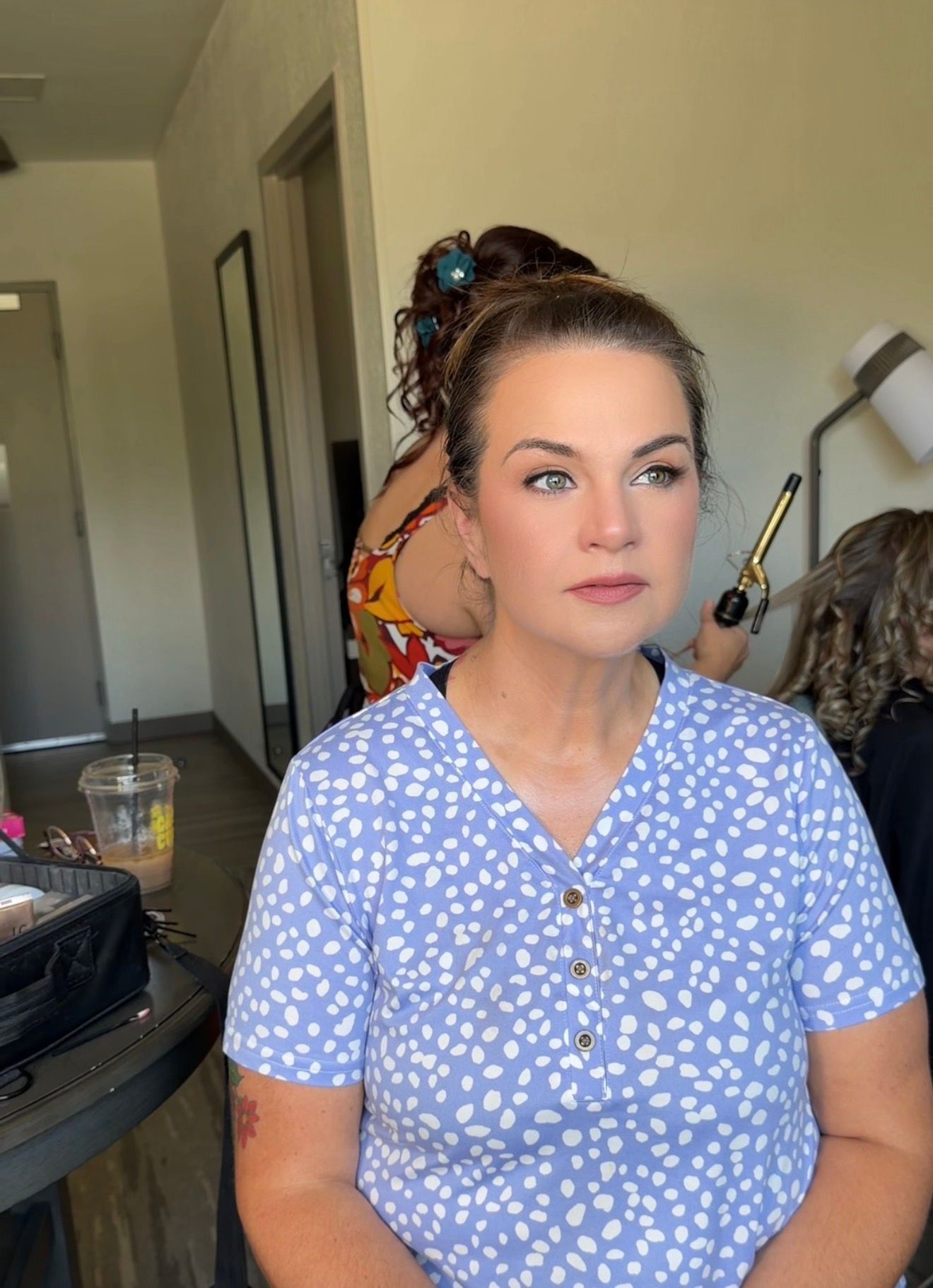 Woman in blue floral dress with updo hairstyle getting ready, likely for a special occasion or wedding.