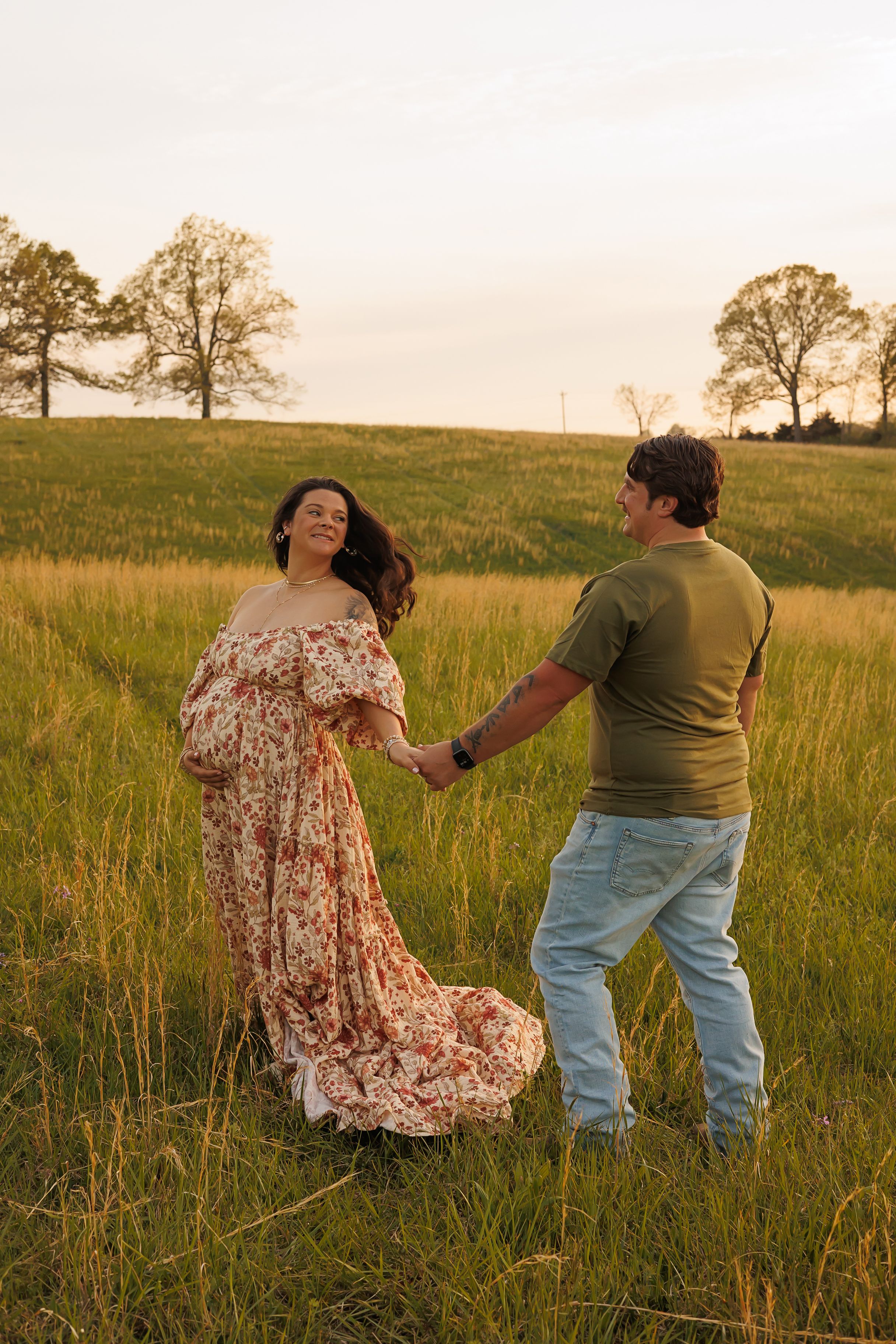Couple dancing together in a meadow at sunset while wearing casual attire.