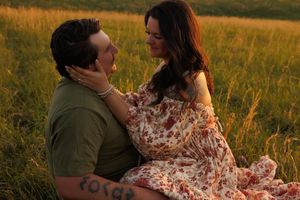 Intimate moment captured between couple sitting in tall grass during sunset.