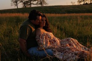 Couple embracing in tall grass field during golden hour sunset.